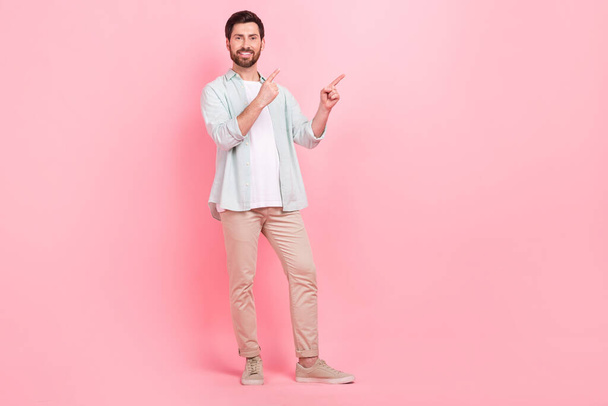 Full size photo of attractive young man hands fingers point empty space wear trendy blue outfit isolated on pink color background. - Foto, afbeelding