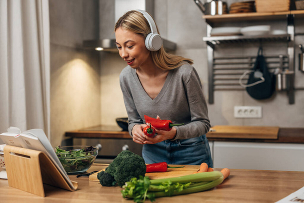 Happy young woman is listening to music and cooking - Foto, Bild