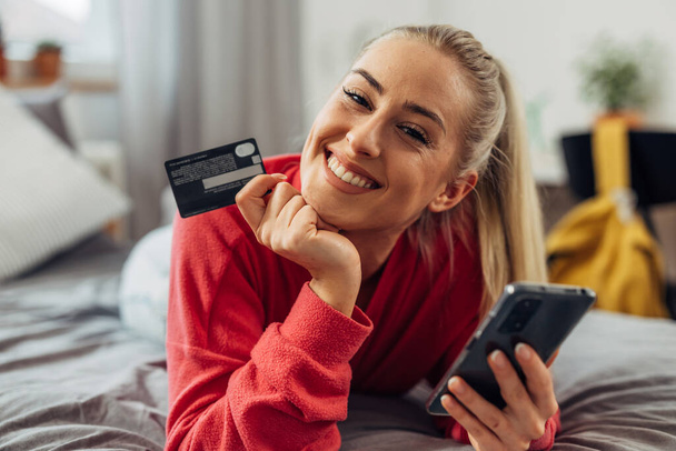 Pretty Caucasian woman is looking at the camera with a credit card in her hand for online shopping - Foto, afbeelding