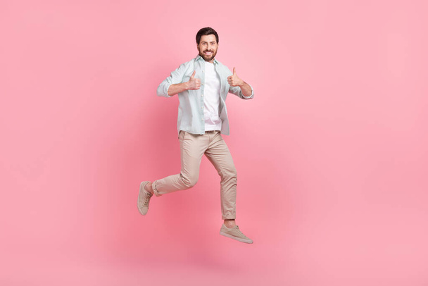 Full length photo of cool confident guy dressed teal shirt jumping high thumbs up isolated pink color background. - Φωτογραφία, εικόνα
