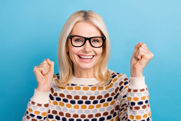 Photo of pretty lucky lady dressed pullover eyewear rising fists screaming yes isolated blue color background. - Φωτογραφία, εικόνα