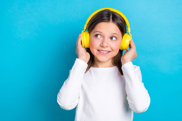 Photo of optimistic satisfied girl wear white long sleeve look empty space arms touching headphones isolated on blue color background. - Foto, Imagem