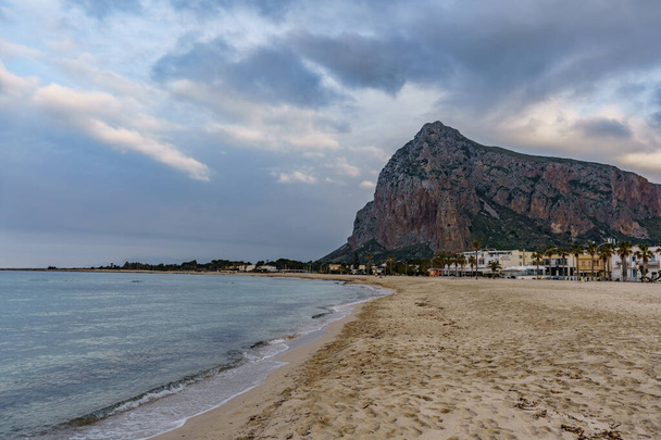 View of a beautiful Sicilian beach with a rocky mountain in the background at the setting sun. - Photo, image