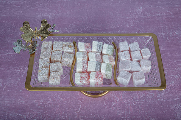 Turkish delight, Turkish delight, on a crystal glass plate. Pink wooden background. Still life, food and drink, seasonal and holiday (ramadan, sugar eid) concept. - Photo, Image
