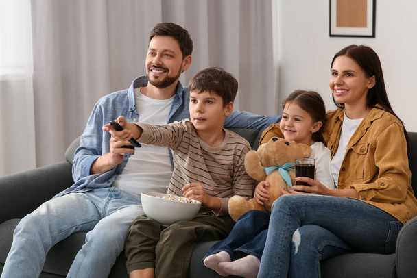 Szczęśliwa rodzina ogląda telewizję w domu. Syn zmienia kanały za pomocą pilota - Zdjęcie, obraz
