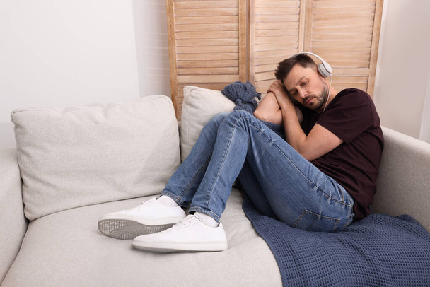 Upset man listening to music through headphones on sofa at home. Loneliness concept - Foto, afbeelding