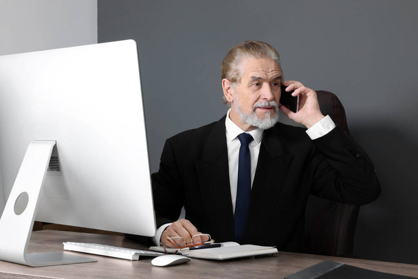 Senior boss talking on phone at wooden table in modern office - Foto, Imagem