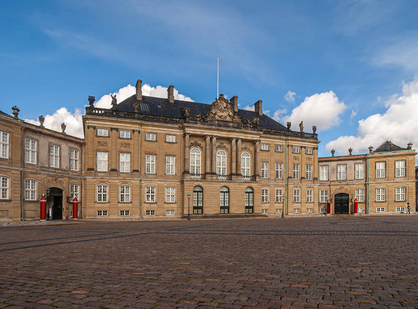 Copenhagen, Denmark - September 13, 2010: King Christian 8 brown stone palace with black roof at Amalienborg square under blue sky. Statues, pillars and windows. Red guard stations add color - Foto, imagen