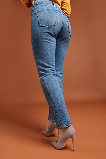 Vrouw in stijlvolle jeans op bruine achtergrond, close-up - Foto, afbeelding