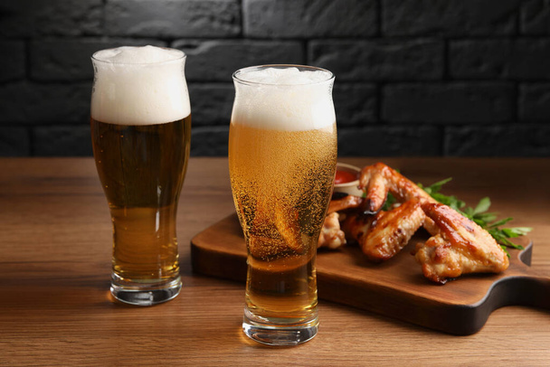 Glasses with beer and delicious baked chicken wings on wooden table - Foto, imagen