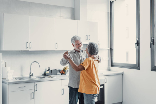 Joyful active old retired romantic couple dancing laughing in living room, happy middle aged wife and elder husband having fun at home, smiling senior family grandparents relaxing bonding together - Photo, Image
