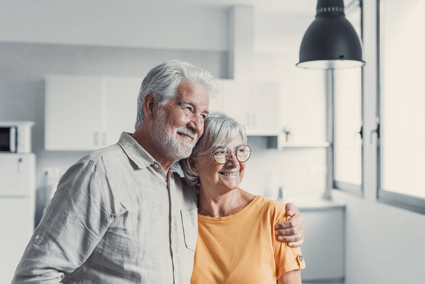 Dreamy middle aged senior loving retired family couple looking in distance, planning common future or recollecting memories, enjoying peaceful moment relaxing together standing in living room - Foto, Bild