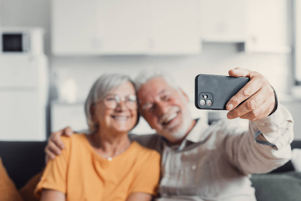 Счастливая пожилая пара делает селфи по мобильному телефону, улыбается пожилые супруги жены среднего возраста и в отставке муж смеется держа телефон сделать автопортрет на смартфоне камеры, сосредоточиться на мобильном дисплее
 - Фото, изображение