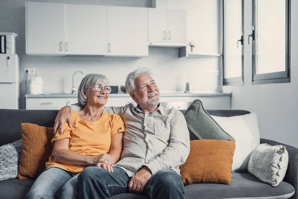 Dreamy middle aged senior loving retired family couple looking in distance, planning common future or recollecting memories, enjoying peaceful moment relaxing together on cozy sofa in living room - Fotoğraf, Görsel