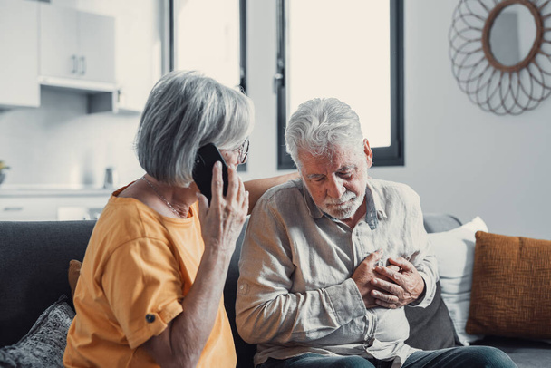 Starsza kobieta, żona wzywająca pogotowie, rozmawiając przez telefon, trzymając stary ręka męża, siwy człowiek o ataku serca, dotykając klatki piersiowej, cierpiących na choroby serca w domu, uczucie bólu - Zdjęcie, obraz