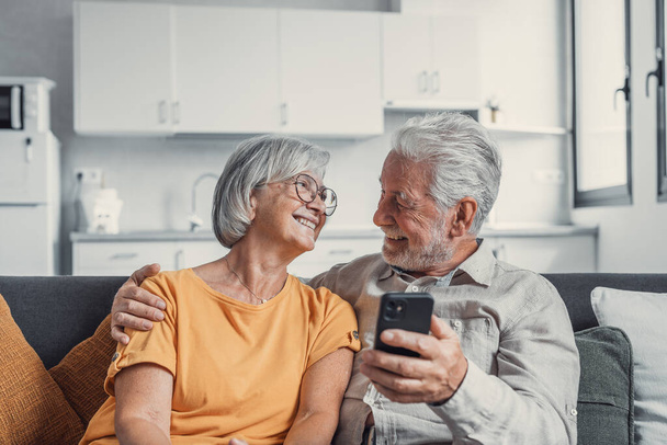 Счастливая зрелая семья, жена и муж с помощью телефона вместе дома, улыбающийся мужчина и женщина среднего возраста, сидя на диване, используя мобильные приложения устройства, смотреть видео в социальной сети, серфинг Интернет
 - Фото, изображение