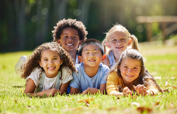 Portrait, smile and children lying on grass in nature on vacation outdoor for learning. Kids, diversity and happiness of group enjoying summer holiday at park or garden, bonding or relaxing together - Foto, Bild