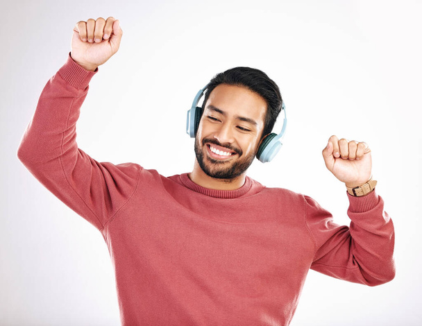 Headphones, happy and man dancing in a studio to music, playlist or album for entertainment. Happiness, dance and Indian male model moving to the radio or streaming a song by a white background - Foto, Imagen