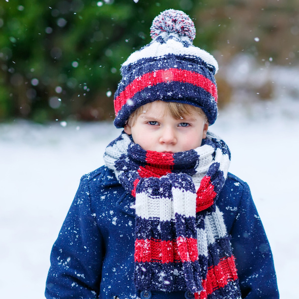 Trieste jongen jongen in kleurrijke winterkleren met plezier met sneeuw, die - Foto, afbeelding