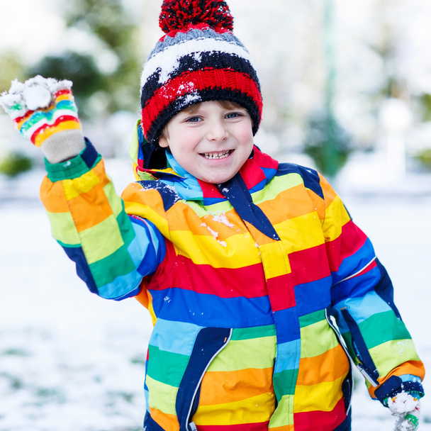 Petit garçon en vêtements d'hiver colorés jouant avec bonhomme de neige, dehors
 - Photo, image