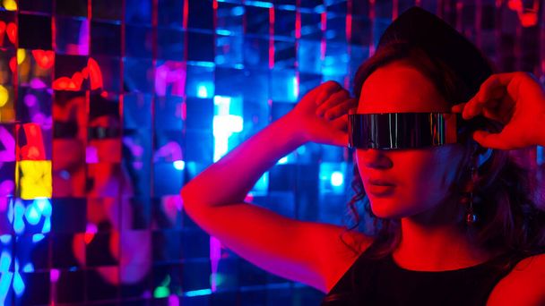 Close-up portrait of a caucasian woman in sunglasses in neon light against a mirror wall - Fotografie, Obrázek