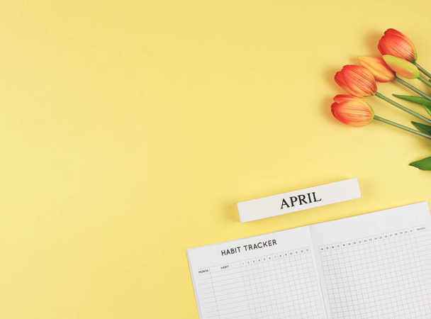 Visão superior ou layout plano do livro de rastreador de hábitos, calendário de madeira de abril e tulipas em fundo amarelo com espaço de cópia. - Foto, Imagem