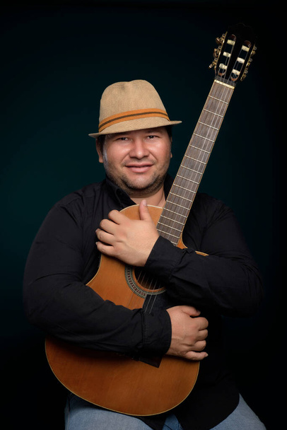 Studio portrait of man wearing hat and holding a guitar - Foto, imagen
