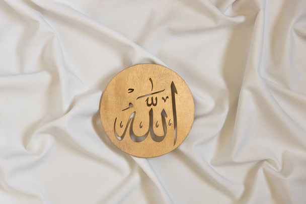 Nombres de Allah bismillah. Caligrafía dorada de madera del dios islam. sobre textil blanco, vista superior - Foto, Imagen