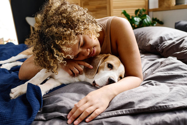 Africana chica con el pelo rizado abrazando con su precioso perro en la cama en el dormitorio - Foto, Imagen
