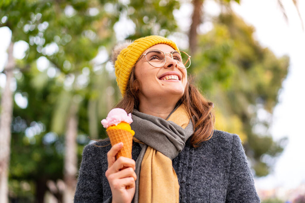 Брюнетка с корнетным мороженым на открытом воздухе смотрит вверх, улыбаясь - Фото, изображение