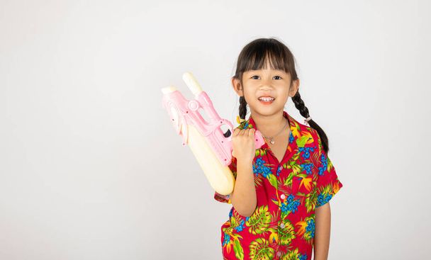 Happy Songkran Day, Asian kid girl with floral shirt hold water gun, Thai child funny hold toy water pistol and smile, isolated on white background, Thailand Songkran festival national culture concept - 写真・画像