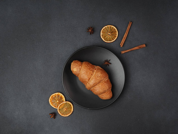 Top view of a delicious, freshly baked Croissant Lying on a black Plate against a black background - 写真・画像