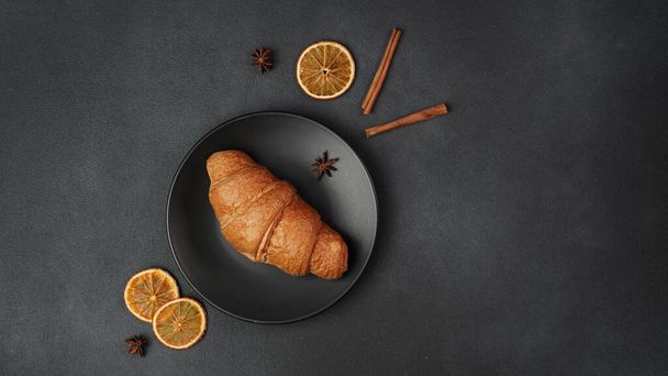 Top view of a delicious, freshly baked Croissant Lying on a black Plate against a black background - 写真・画像