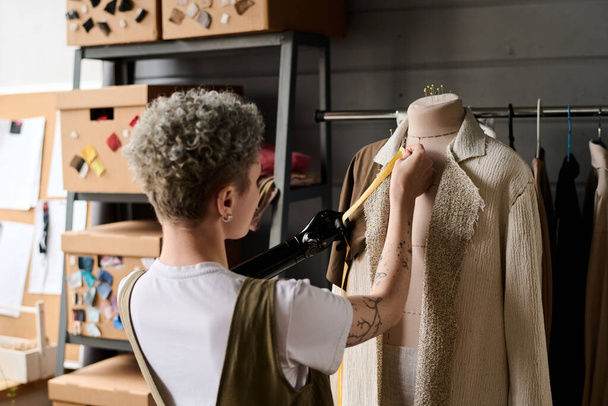 Vue arrière de jeunes couturiers prenant des mesures de manteau beige sur mannequin tout en travaillant sur un nouvel ordre de client en atelier - Photo, image
