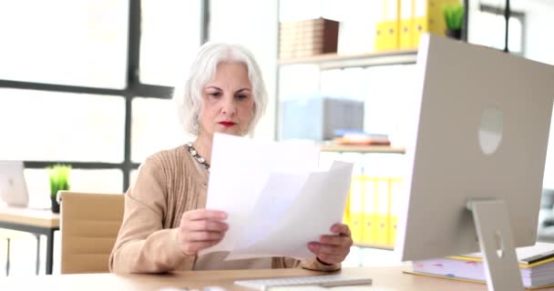 Fiduciosa donna d'affari anziana che lavora con laptop e documenti in carica. Senior SEO esamina i documenti finanziari - Filmati, video