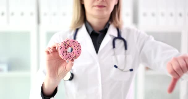 Dietista doctora sosteniendo rosquilla dulce y signo negativo con la mano. Daño de los dulces en la salud de la piel y los dientes - Metraje, vídeo