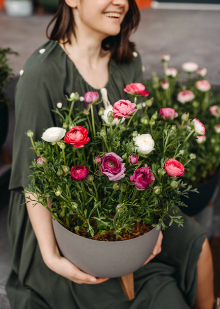 Mujer en una florería sosteniendo una maceta grande con flores de ranúnculo rosa, primer plano. - Foto, imagen