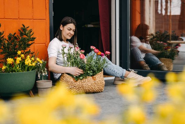 Florist working at a flower shop. Woman taking care of us flowers, arranging them into a big basket. - Foto, Imagem