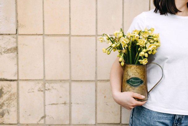 Primo piano di una donna che tiene un vaso con piccoli fiori narcisi. - Foto, immagini