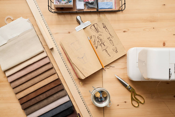 布サンプルと木製テーブルの角度、スケッチや鉛筆、電動ミシン、定規やはさみのノートブックの上 - 写真・画像