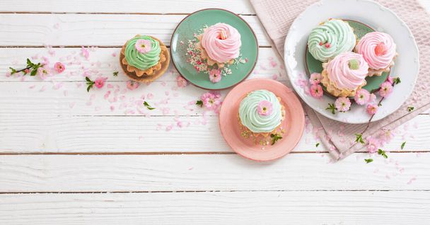 pink and green cupcakes with spring flowers on white wooden background - Foto, afbeelding