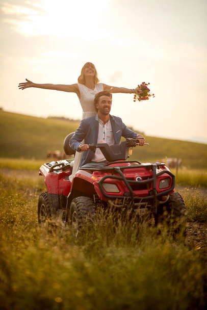 Young newlyweds are enjoying the scenery while riding the quad on a beautiful sunny day in the nature. Riding, nature, wedding, activity - Foto, afbeelding