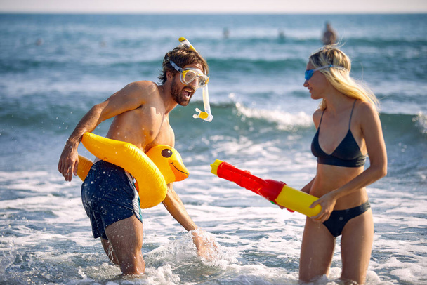 Happy young man and girl  with water toys have fun on the beach by the sea - Foto, imagen