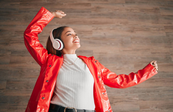 Woman, happiness and dancing with music headphones isolated on a wood background. Freedom, dance and female or person listening, streaming or enjoying audio, radio song or podcast, sound and smile - Photo, Image
