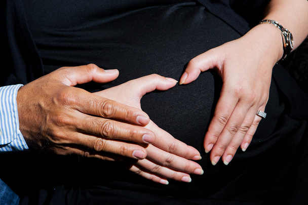 Nahaufnahme einer schwangeren Frau, die ihre Hände auf ihrem geschwollenen Bauch hält - Foto, Bild