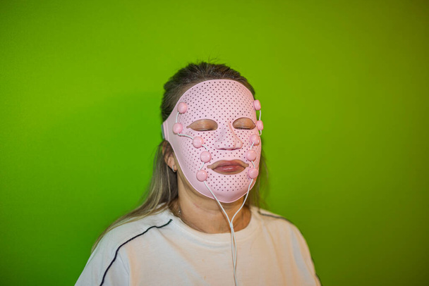 Yeşil arka planda pembe maske takmış, gözleri kapalı bir kadının yakın görüntüsü. İsveç. - Fotoğraf, Görsel