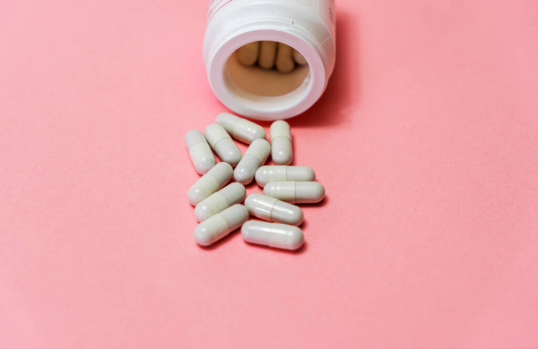 Pills spilled out of white bottle on pink background. Mock up for special offers as advertising or other ideas. Medical, pharmacy and healthcare concept. Copy space. Empty place for text or logo - Photo, Image