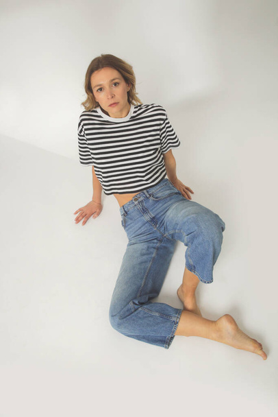 Fashion portret van jonge vrouw in ontspannen brede jeans en gestreepte t-shirt op de witte achtergrond - Foto, afbeelding
