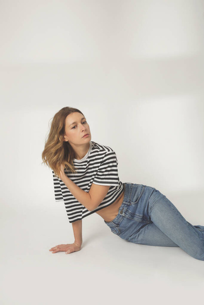 Fashion portrait of young woman in relaxed wide jeans and striped t shirt on the white background - Photo, image