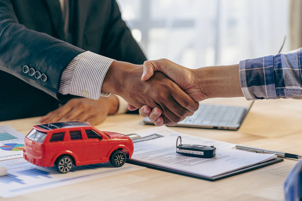 Biznes samochodowy, sprzedawca samochodów prezentujący samochód nowemu właścicielowi i podający dłonie podczas gratulacji dwóm klientom - Zdjęcie, obraz